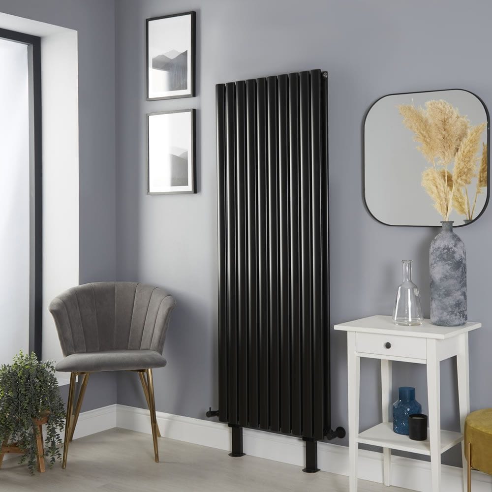 Milano Aruba black vertical designer radiator with feet on light wall nearby mirror and two framed art pictures above grey chair
