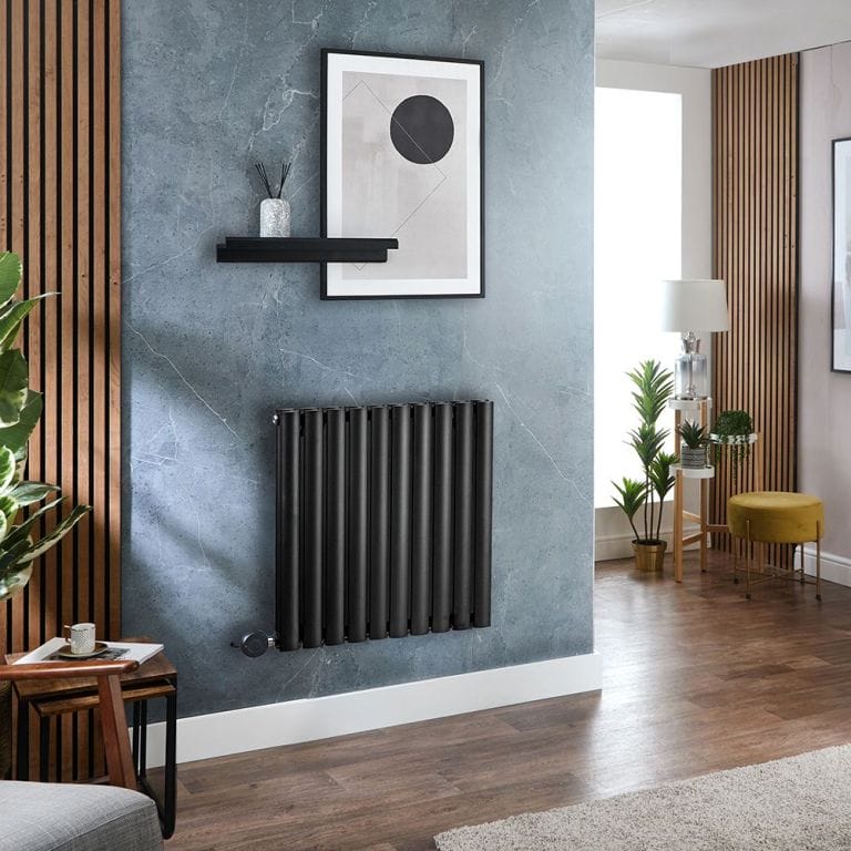Milano x ECOSO Aruba electric black horizontal designer radiator on blue wall beneath framed artwork and small black shelf nearby wooden panelling