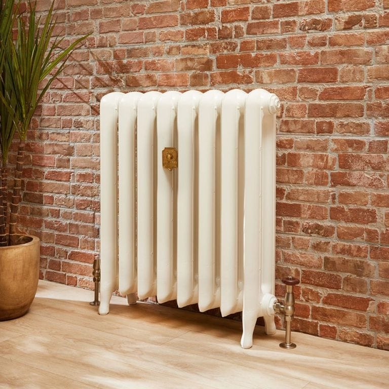 Milano Tamara white oval cast iron column radiator in front of brick-effect wall nearby houseplant