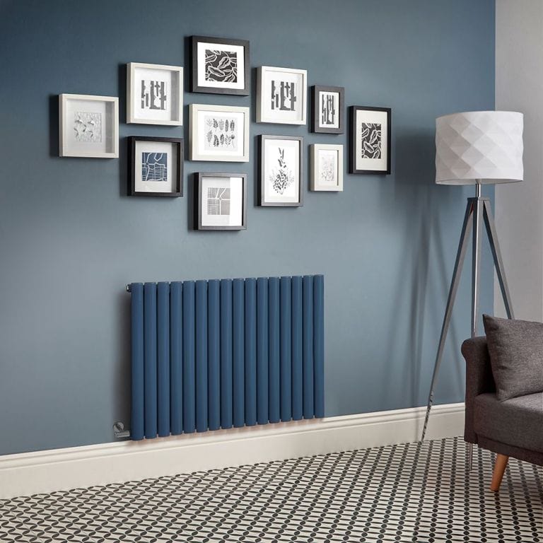 Milano Aruba electric deep sea blue horizontal designer radiator on blue wall beneath multiple framed pictures nearby freestanding lamp and charcoal settee