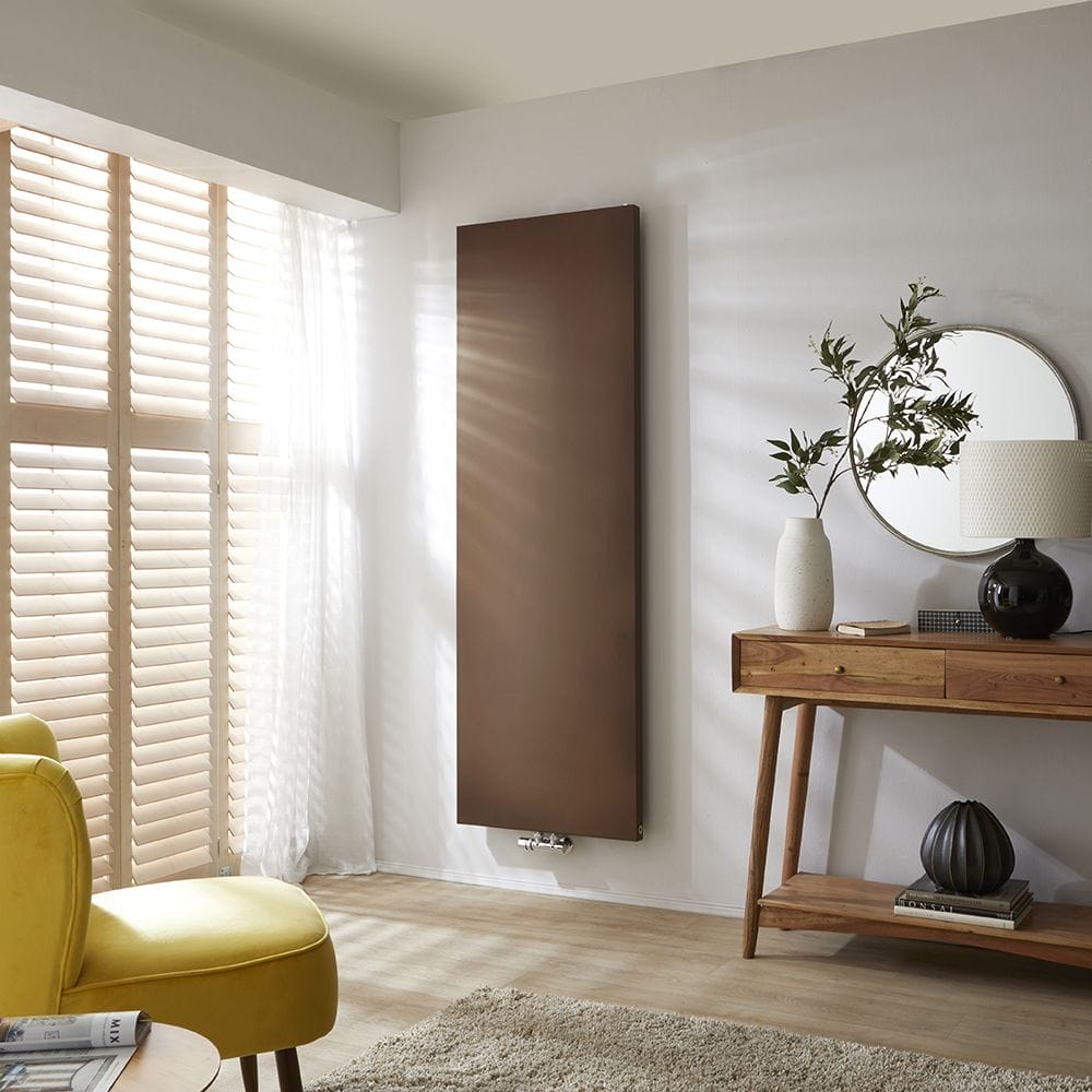 Milano Riso antique copper flat panel vertical designer radiator on white wall in minimalist interior nearby blinds and table with vase and lamp