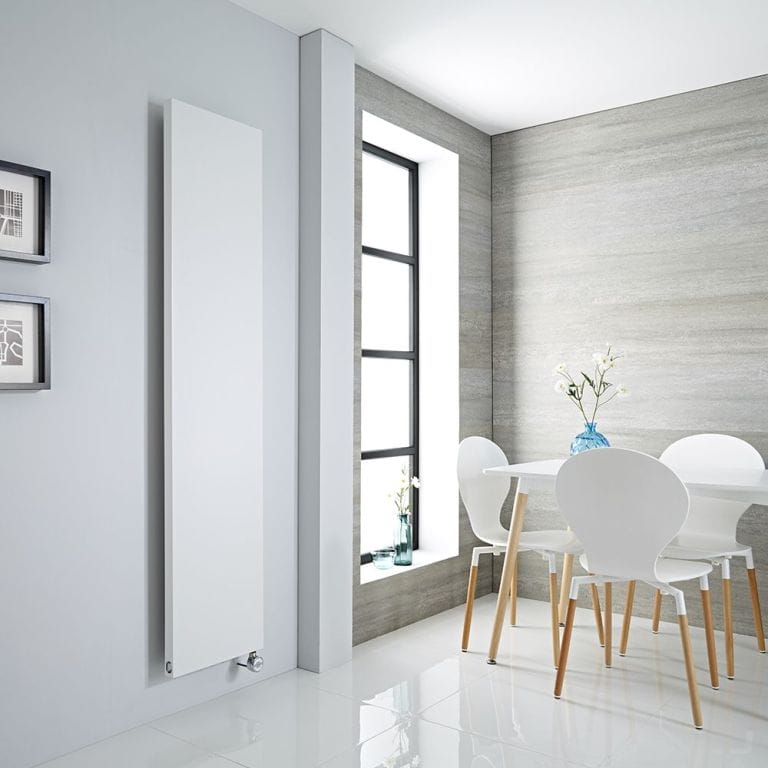 Milano x ECOSO Riso white electric flat panel vertical designer radiator on white wall nearby white table and chairs and vertical window inset from modern grey wall