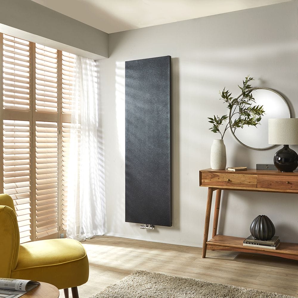 Milano Riso black flat panel designer radiator on white wall nearby blinds and table with lamp, vase and mirror