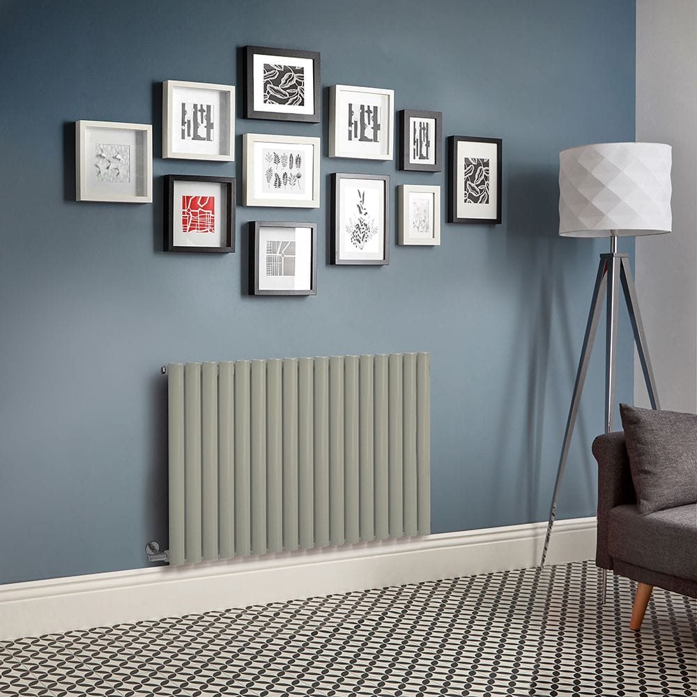 Milano Aruba electric sage leaf green horizontal designer radiator on light blue wall beneath multiple pieces of framed artwork nearby tall lamp