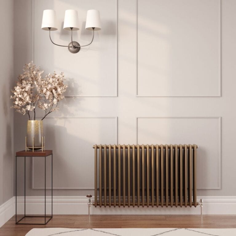 Milano Windsor metallic bronze horizontal triple column traditional designer radiator on light wall nearby table with gold vase and artificial plant beneath triple light fitting