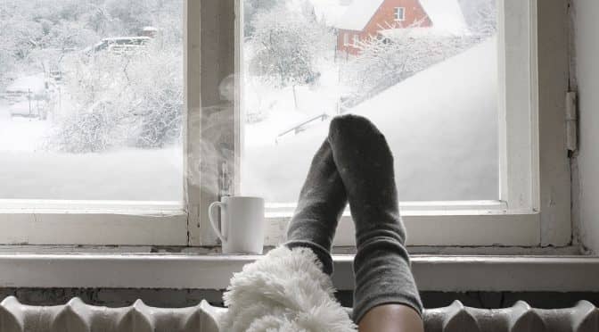 A woman's feet raised up on to a radiator with snow visible through a window