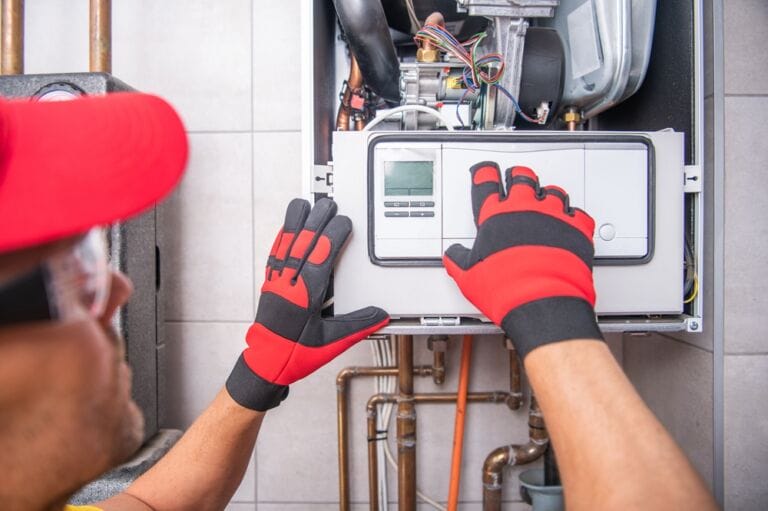 Heating technician in red cap and red and black gloves repairing gas boiler repair work in domestic setting