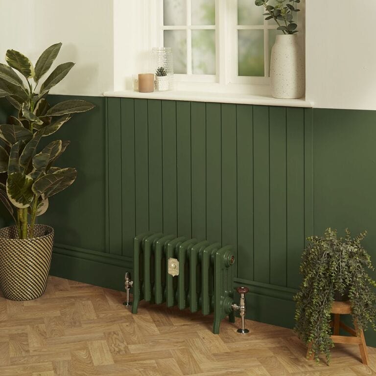 Milano Isabel 4 column cast iron radiator in Farriw & Ball duck green on hardwood floor in front of a green wall and in between a pair of green houseplants