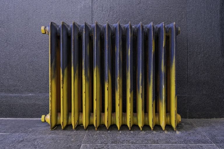 Retro blue and yellow radiator with worn-out effect on grey flooring and background