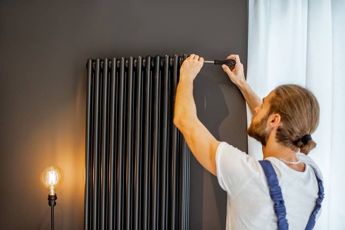 Handyman releasing trapped air from black hot water radiator