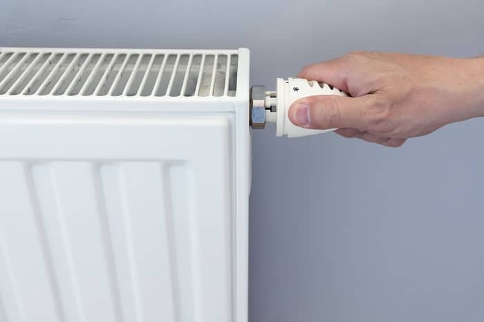 Hand adjusting valve on white convector radiator against blue background