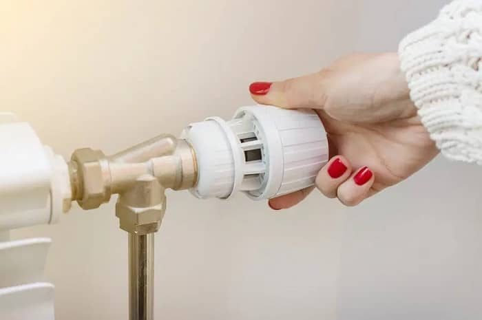 a woman turning a thermostatic radiator valve on a heating appliance