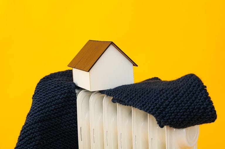 Small white wooden house with brown roof on top of white radiator with navy scarf and yellow background