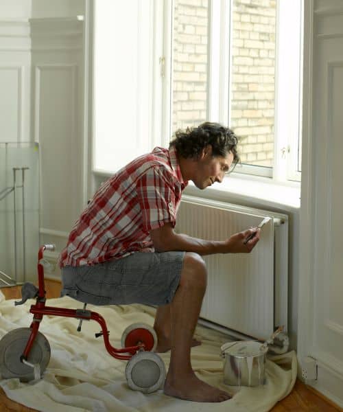 man sat on a stool painting a radiator