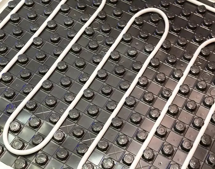 White electric underfloor heating wires on black surface Close up image of white electric underfloor heating wiring on black surface