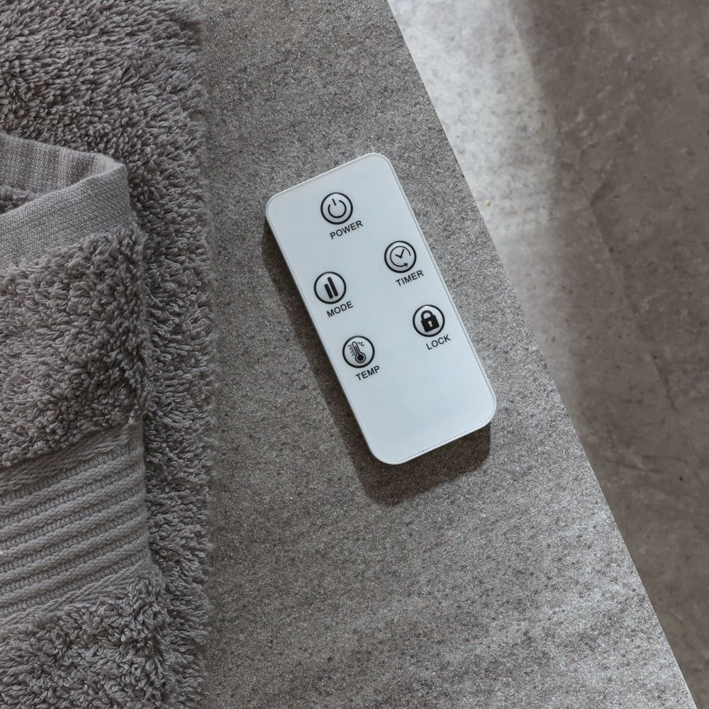 White fan electric towel rail remote ECOSO white smart electric heated towel rail with fan remote on settee next to grey towel