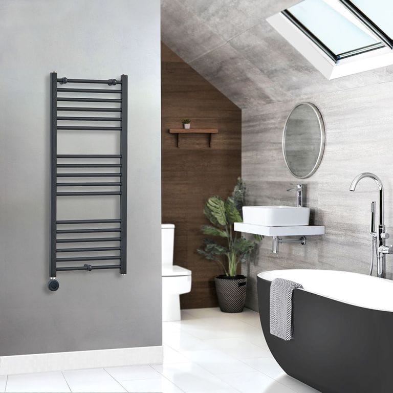 Milano x ECOSO Artle electric curved anthracite heated towel rail on grey wall in modern bathroom setting nearby black and white freestanding tub with chrome tub filler and circular mirror above white sink on floating white shelf