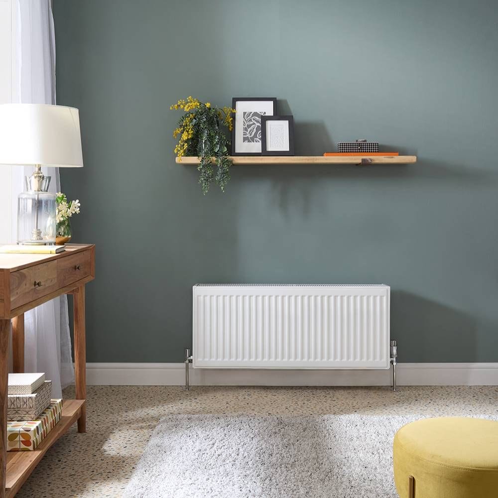 Milano Compact Type 33 white horizontal low level triple panel convector radiator on green wall underneath a shelf with picture frames and plant