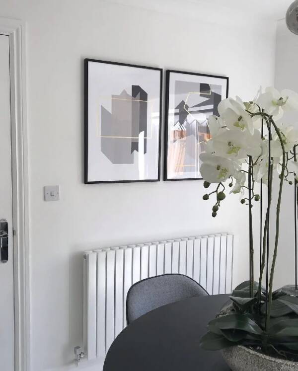White horizontal Milano radiator on white wall A modern white Milano horizontal designer radiator on a white wall beneath framed art