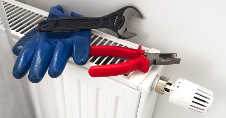 Radiator with thermostat, adjustable spanner and pliers and blue gloves positioned on top