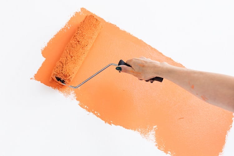 a warming orange colour being painted onto a wall with a paint roller a warming orange colour being painted onto a wall with a paint roller