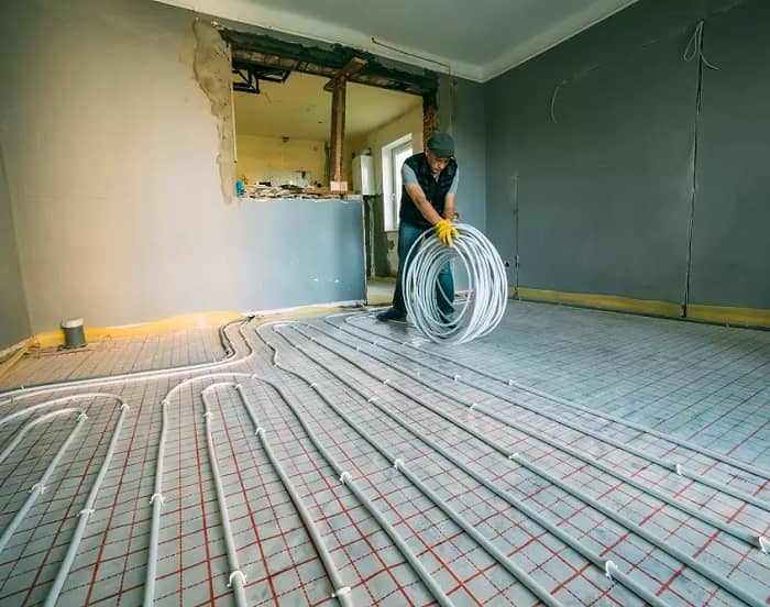 Heating engineer with yellow gloves rolling up white electric wires for underfloor heating