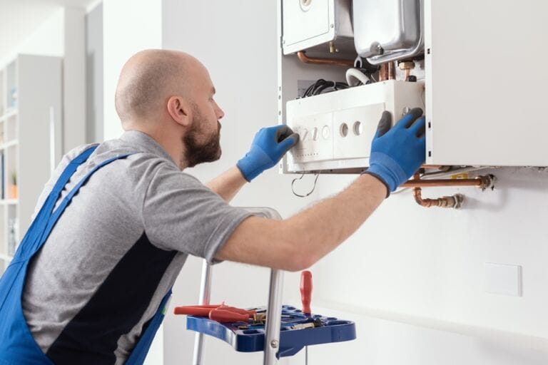 Heating engineer in blue overalls and blue gloves servicing a domestic boiler in home setting