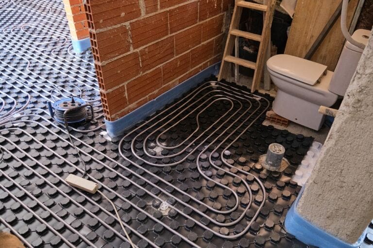 Radiant underfloor heating installation in a bathroom area with brick wall and small ladders and toilet visible