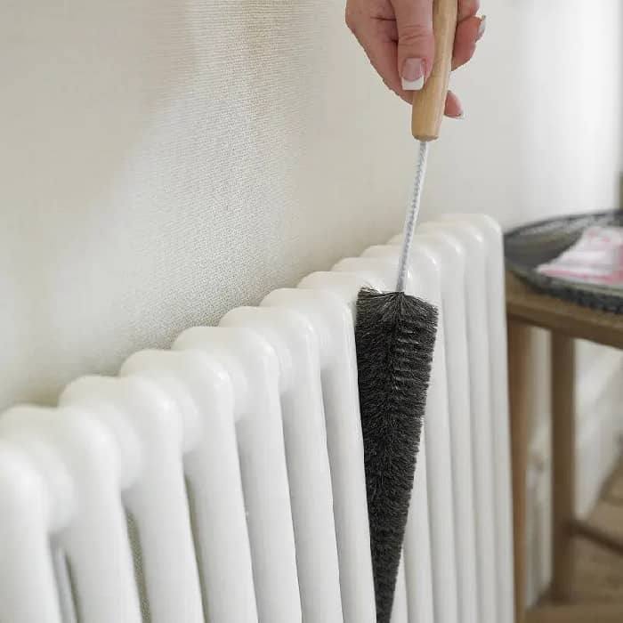 a person using a duster to clean the inside of a radiator
