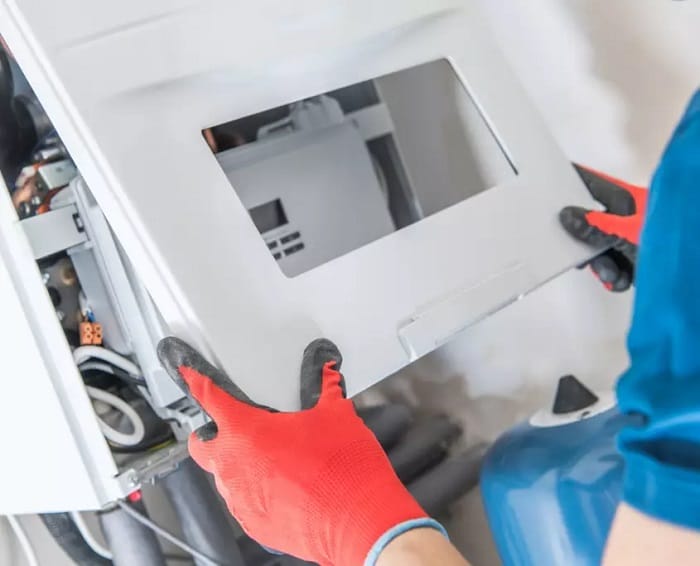 Heating engineer placing boiler shell on boiler Heating engineer with red gloves attaching outer shell of boiler onto boiler system