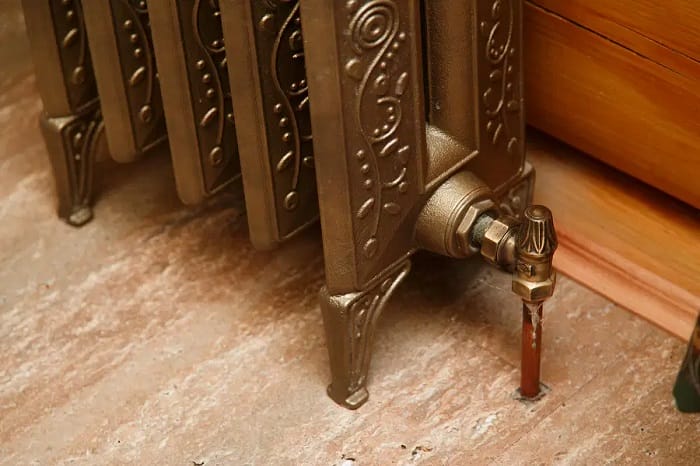 Retro styled cast iron radiator with valve and copper pipe. Close up Close up of radiator valve and rad tail at foot of retro cast iron radiator