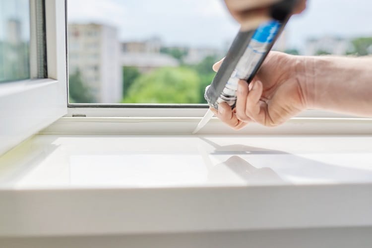 a man sealing up a bathroom window to prevent heat from being lost