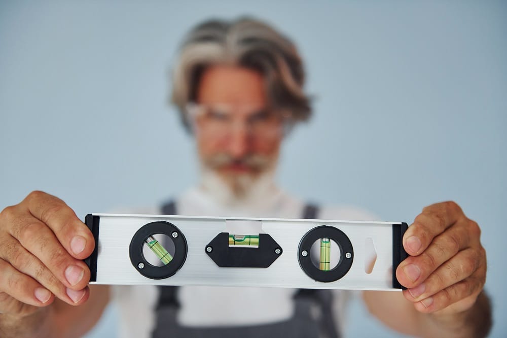 Worker in uniform holds level matching device. Senior stylish modern man with grey hair and beard indoors
