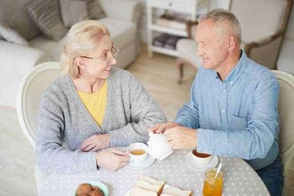An elderly couple having a cup of tea and smiling at each other