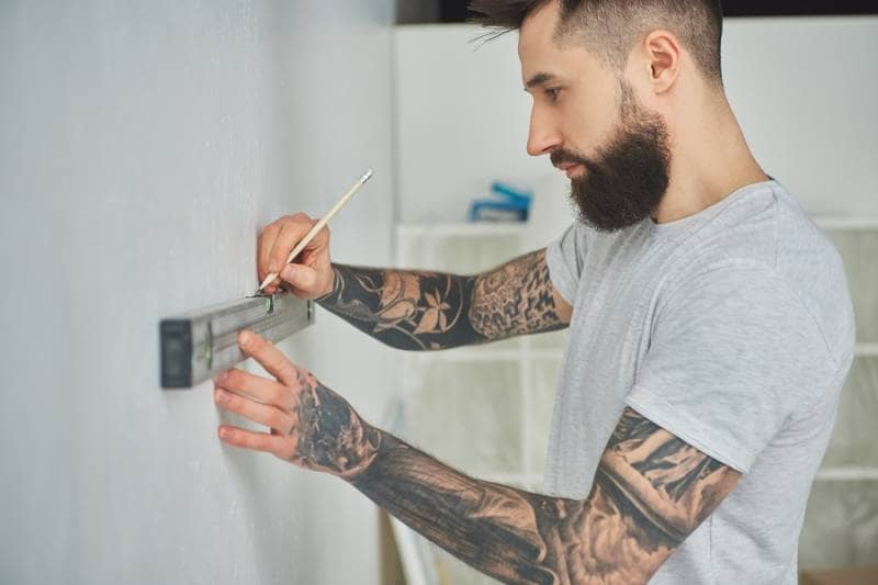 Gold cast iron radiator with pattern Bearded man using spirit level and pencil during home improvement work