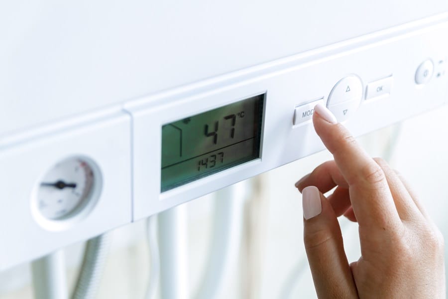 Female hand adjusting boiler settings with temperature shown on digital display