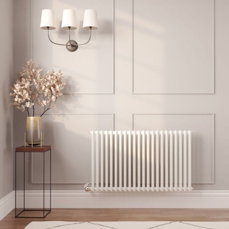 Milano Windsor white traditional horizontal electric double column radiator on light wall nearby small table with vase and fake houseplant below triple lamp fitting