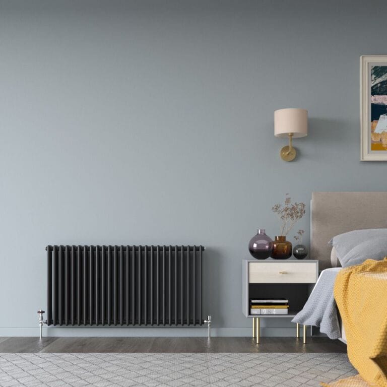 Milano Windsor black horizontal traditional double column radiator on light blue wall nearby bedside table and lamp and bed beneath artwork