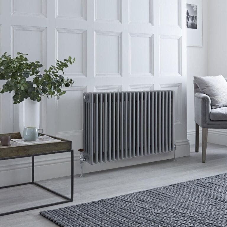 Milano Windsor anthracite traditional horizontal four column radiator on white wall nearby table with vase and houseplant and grey chair
