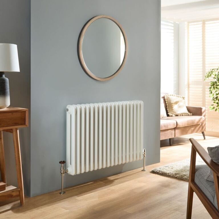 Milano Atticus white horizontal modern column radiator on wooden flooring in front of light wall beneath a circular mirror in a modern home