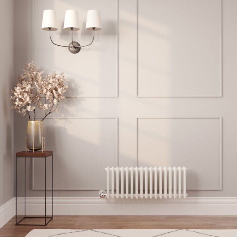 Milano Windsor white traditional triple column electric radiator on light wall nearby table with gold vase and artificial plant beneath triple light fitting