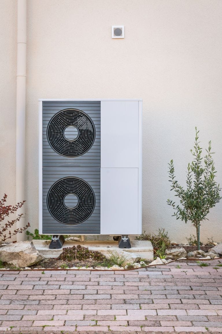 Two white and grey air source heat pumps installed outside a home
