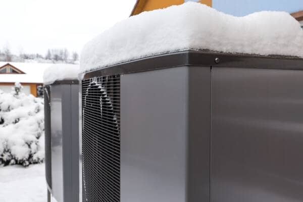 Two modern residential air source heat pumps covered in snow