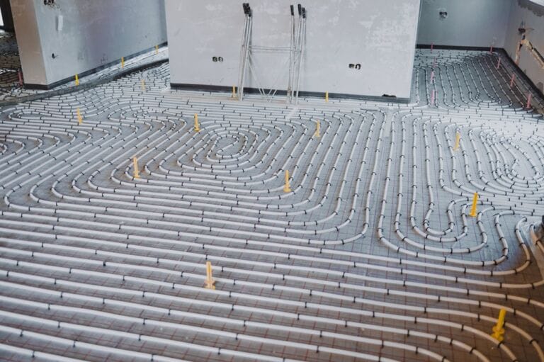 Underfloor heating system installation setup featuring multiple white plastic pipes forming network on the floor
