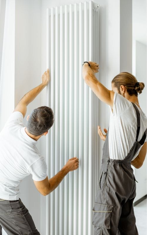 Two handymen adjusting position of white vertical radiator