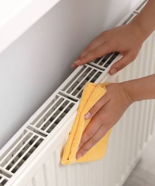 Using a yellow cloth to clean a white convector radiator