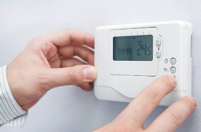 Man switching on a thermostat Close up shot of hands switching on a white thermostat
