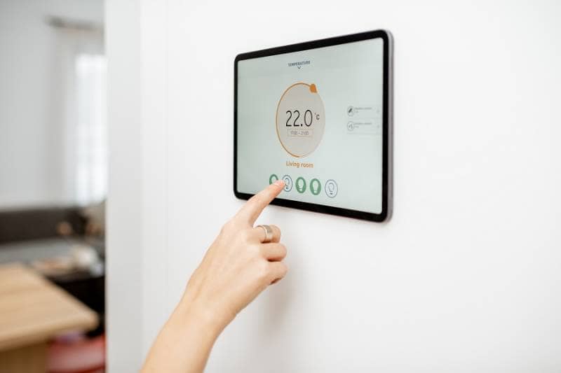 Woman controlling living room temperature with a wall mounted digital touch screen panel linked to a smart heating system