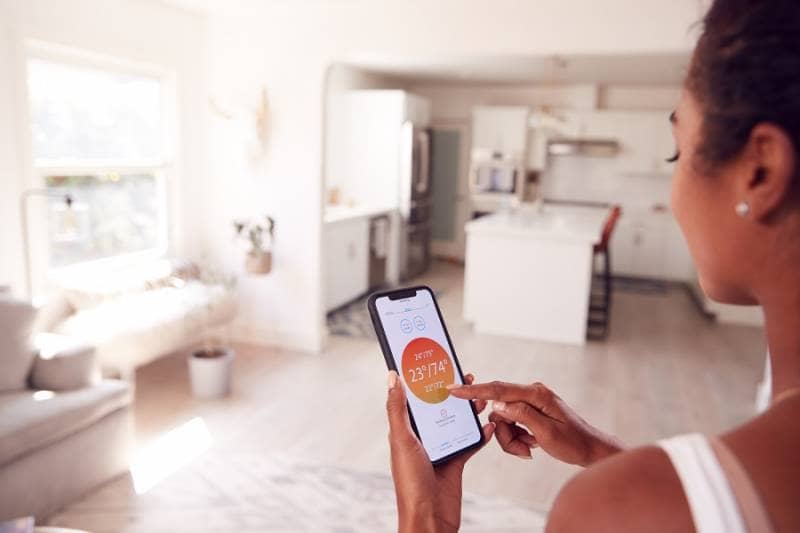 Woman using mobile phone to control smart home heating system