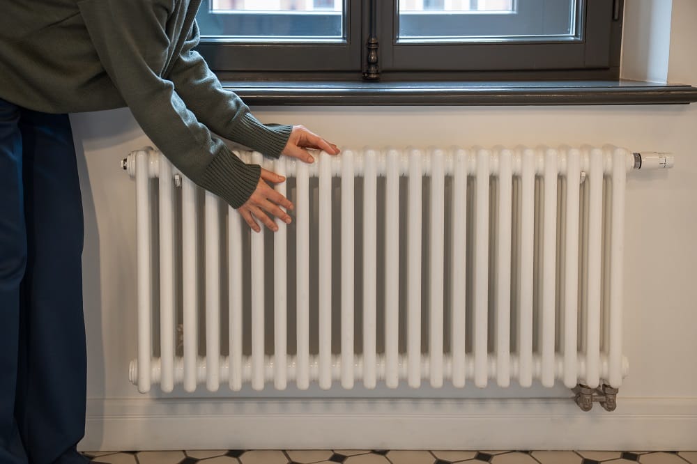 Hands being warrmed on white horizontal radiator positioned beneath a window